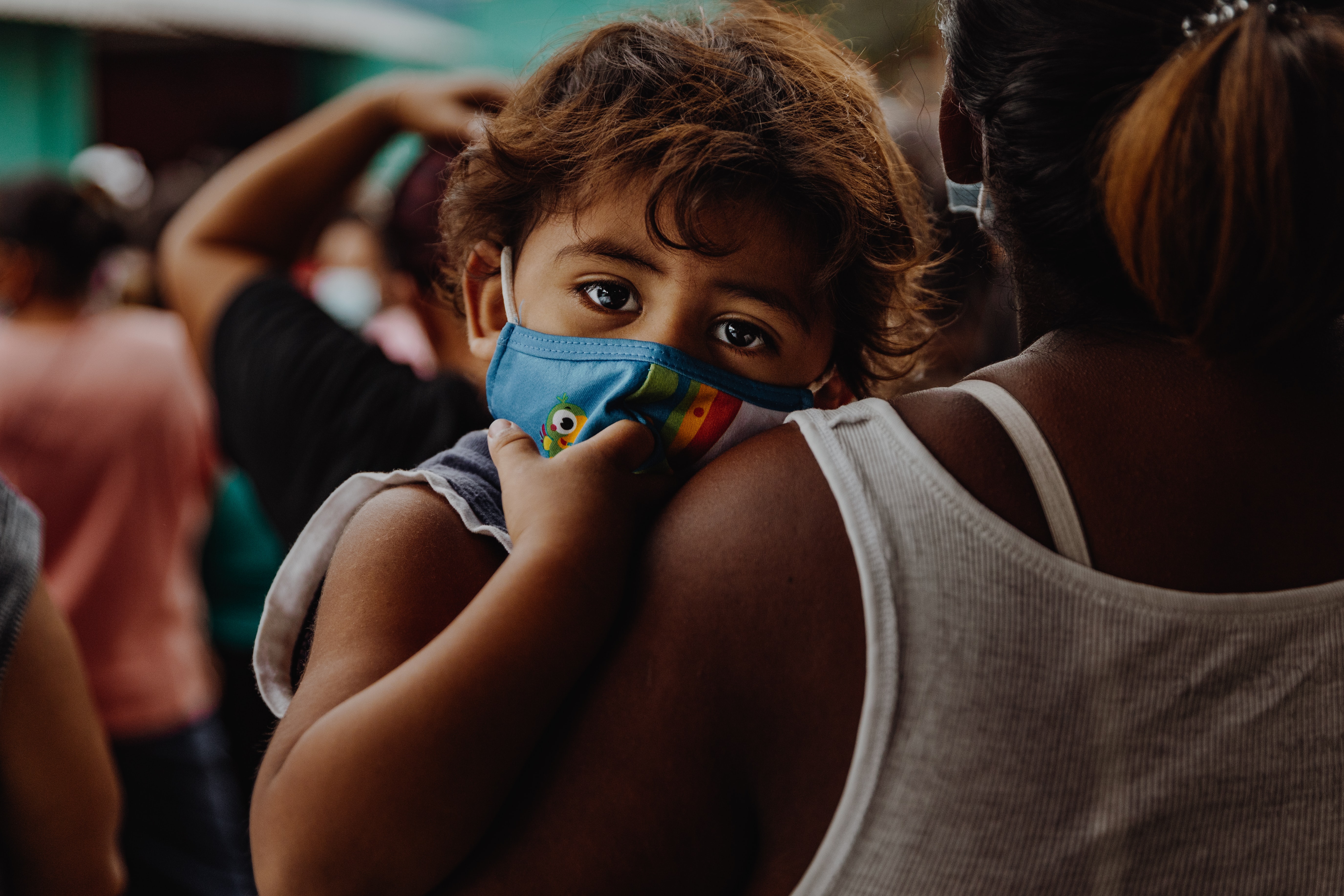 a woman holding a young boy who is wearing a mask and looking at the camera